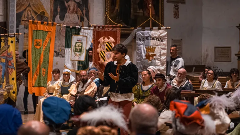 Un attore in costume si rivolge al pubblico davanti ai gonfaloni