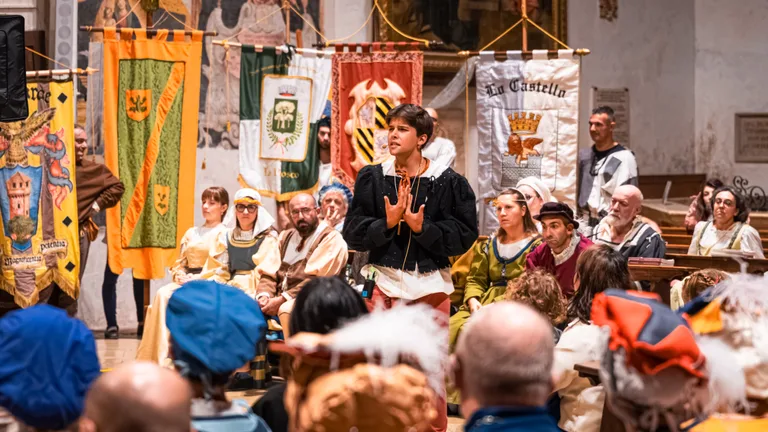 Un attore in costume parla al pubblico tra i gonfaloni delle contrade